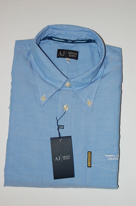 Jasnoniebieska, złożona koszula męska marki Armani Jeans z metką i widocznym logo na kieszeni, leżąca na białym tle.