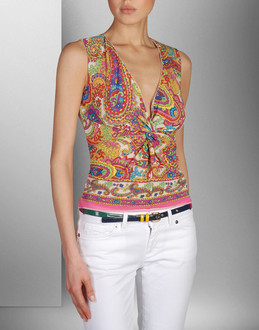 Kobieta prezentuje bluzkę bez rękawów z wzorem paisley, białe spodnie i pasek z ozdobną klamrą.