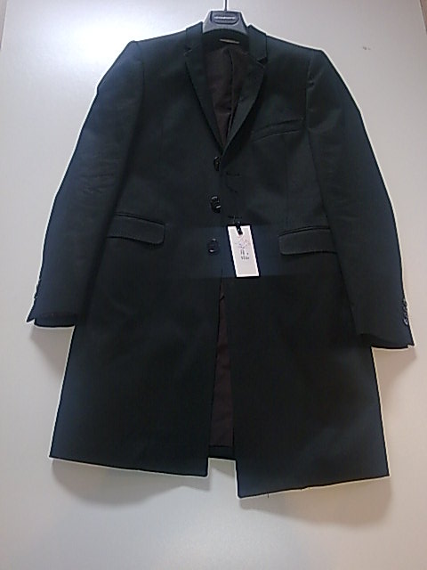 Elegancki, ciemny płaszcz męski na wieszaku, z widoczną metką, prezentowany na jasnym tle.