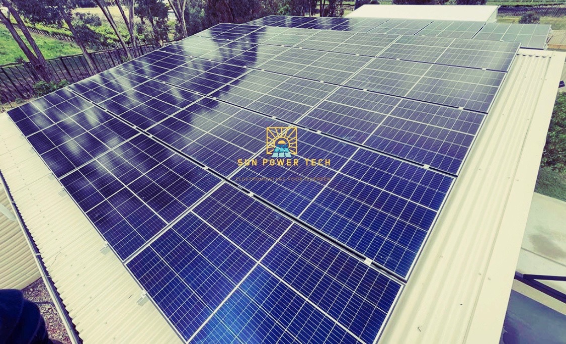 Widok z góry na instalację paneli słonecznych na dachu budynku, z widocznym logo 'Sun Power Tech' na panelach.