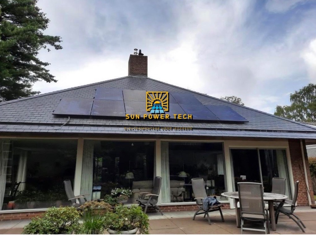 Panele słoneczne na dachu domu jednorodzinnego z szarym dachem, widoczne z poziomu tarasu z meblami ogrodowymi i roślinami w donicach.