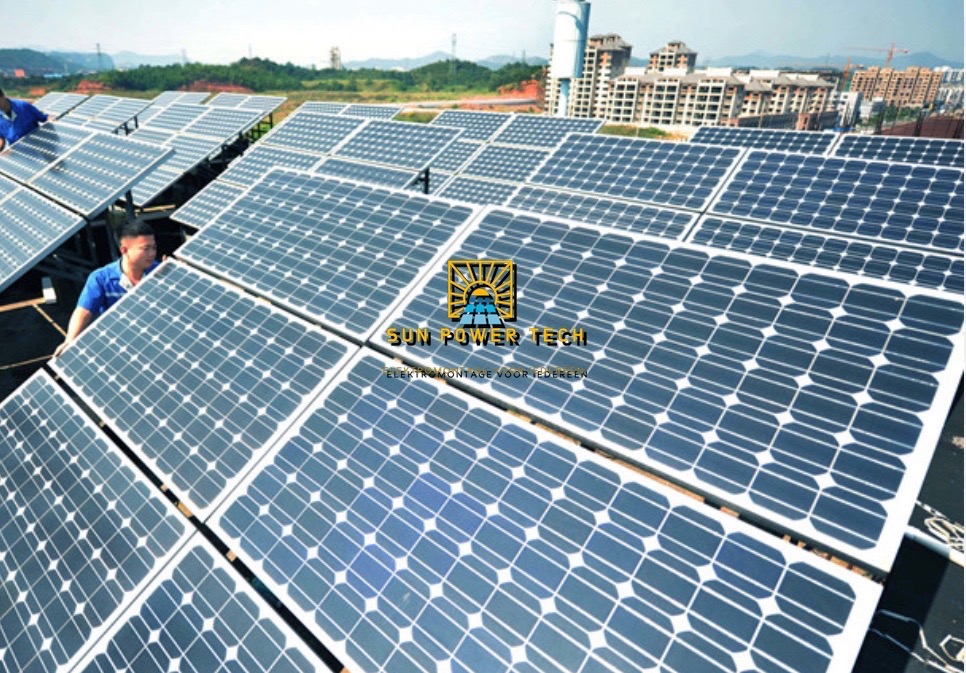 Instalacja paneli słonecznych na dachu budynku, widoczni dwaj monterzy w niebieskich koszulkach, w tle zabudowa miejska i logo firmy na panelach.