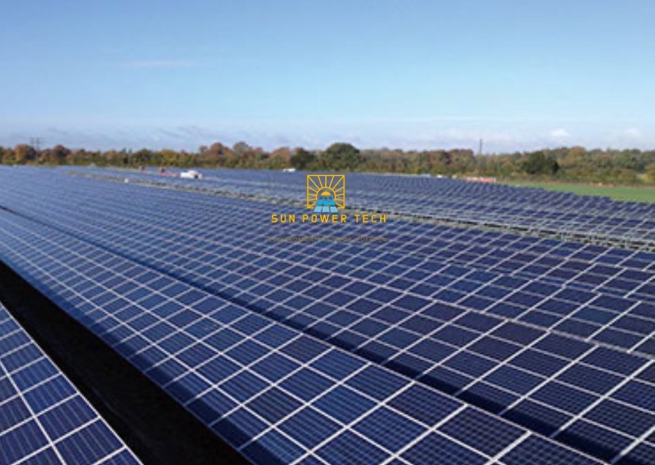 Rozległa farma paneli słonecznych z logo firmy Sun Power Tech w oddali, widoczna z niskiej perspektywy, z zielonymi drzewami w tle pod błękitnym niebem.