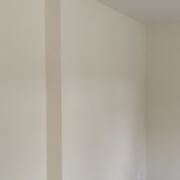 Ambika PL - Świeżo pomalowane, jasne wnętrze w Warszawie z widocznym filarem i podłogą przygotowaną do dalszych prac wykończeniowych. Na podłodze widoczne resztki po remoncie i narzędzia.