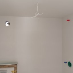 Ambika PL - Białe ściany w łazience w trakcie remontu, widoczne wystające kable ze sufitu, przygotowane podejścia wodno-kanalizacyjne i zabezpieczone elementy armatury.