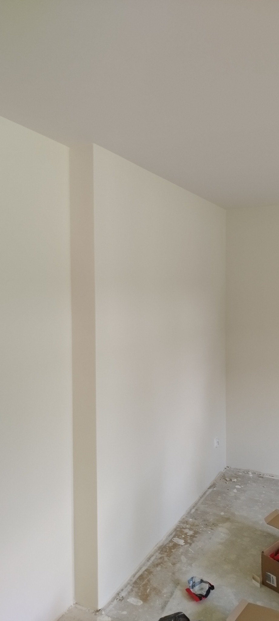 Świeżo pomalowane, jasne wnętrze w Warszawie z widocznym filarem i podłogą przygotowaną do dalszych prac wykończeniowych. Na podłodze widoczne resztki po remoncie i narzędzia.