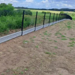 Nowoczesne ogrodzenie panelowe z podmurówką betonową na tle zieleni i błękitnego nieba z chmurami.