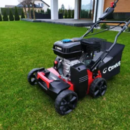 Nowoczesna kosiarka spalinowa marki Cedrus na tle idealnie przystrzyżonego, soczyście zielonego trawnika przed minimalistycznym domem.