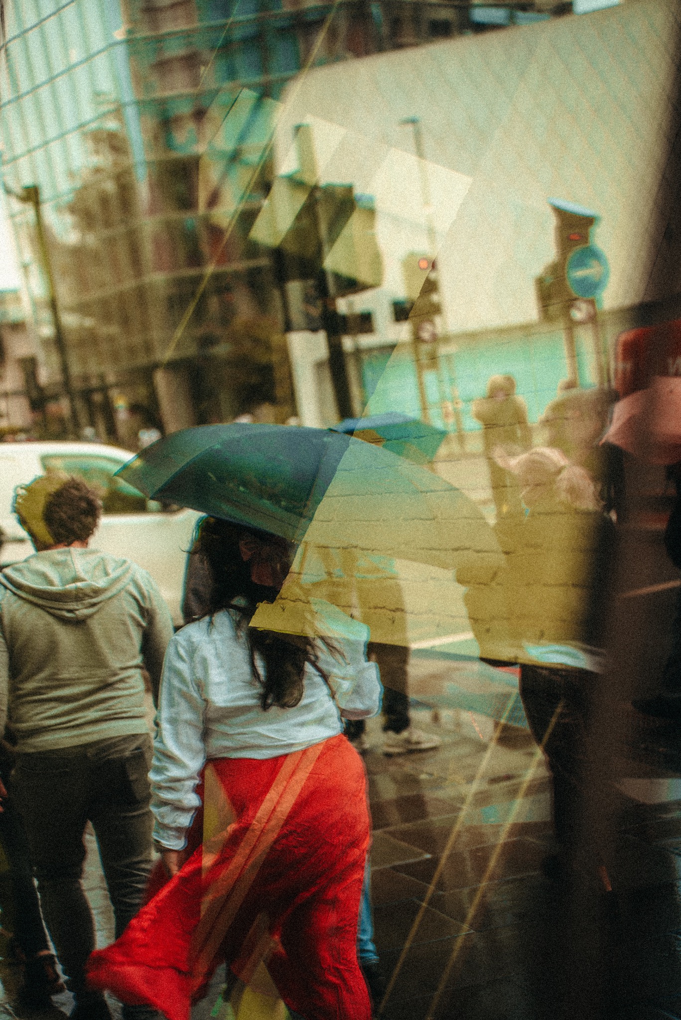 Uliczny kadr ze Świdwina: ludzie z parasolami w deszczowy dzień, odbicie w szybie tworzy artystyczny efekt.