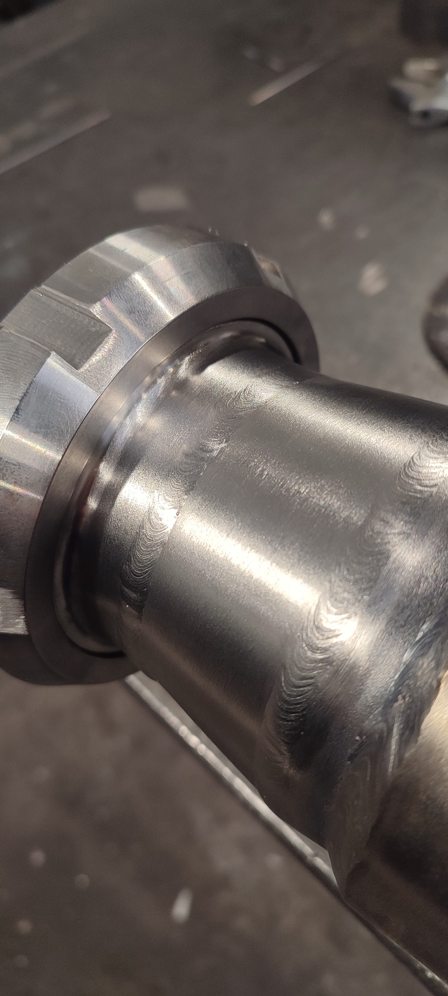 Szlifowany spaw na metalowej rurze z kołnierzem, widoczne ślady obróbki i delikatne refleksy światła. Precyzyjne połączenie elementów.