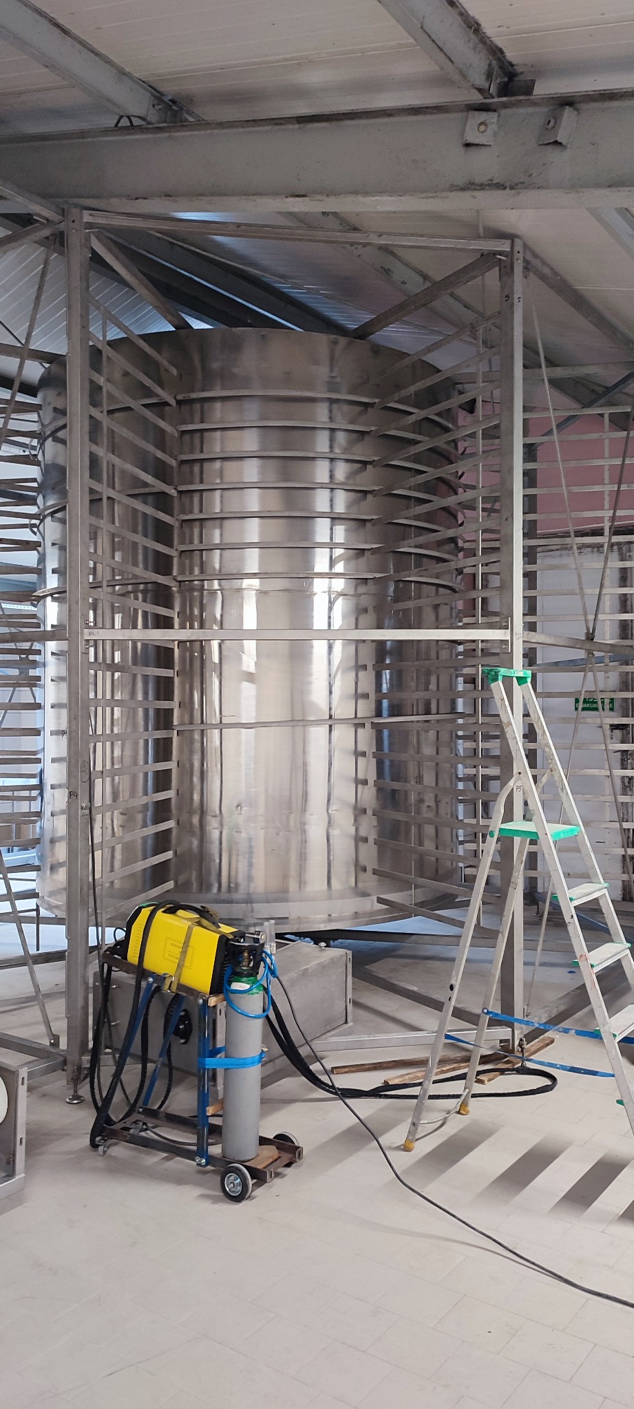 Konstrukcja ze stali nierdzewnej w hali produkcyjnej, widoczny sprzęt spawalniczy i drabina. Elementy konstrukcyjne spawane na miejscu.