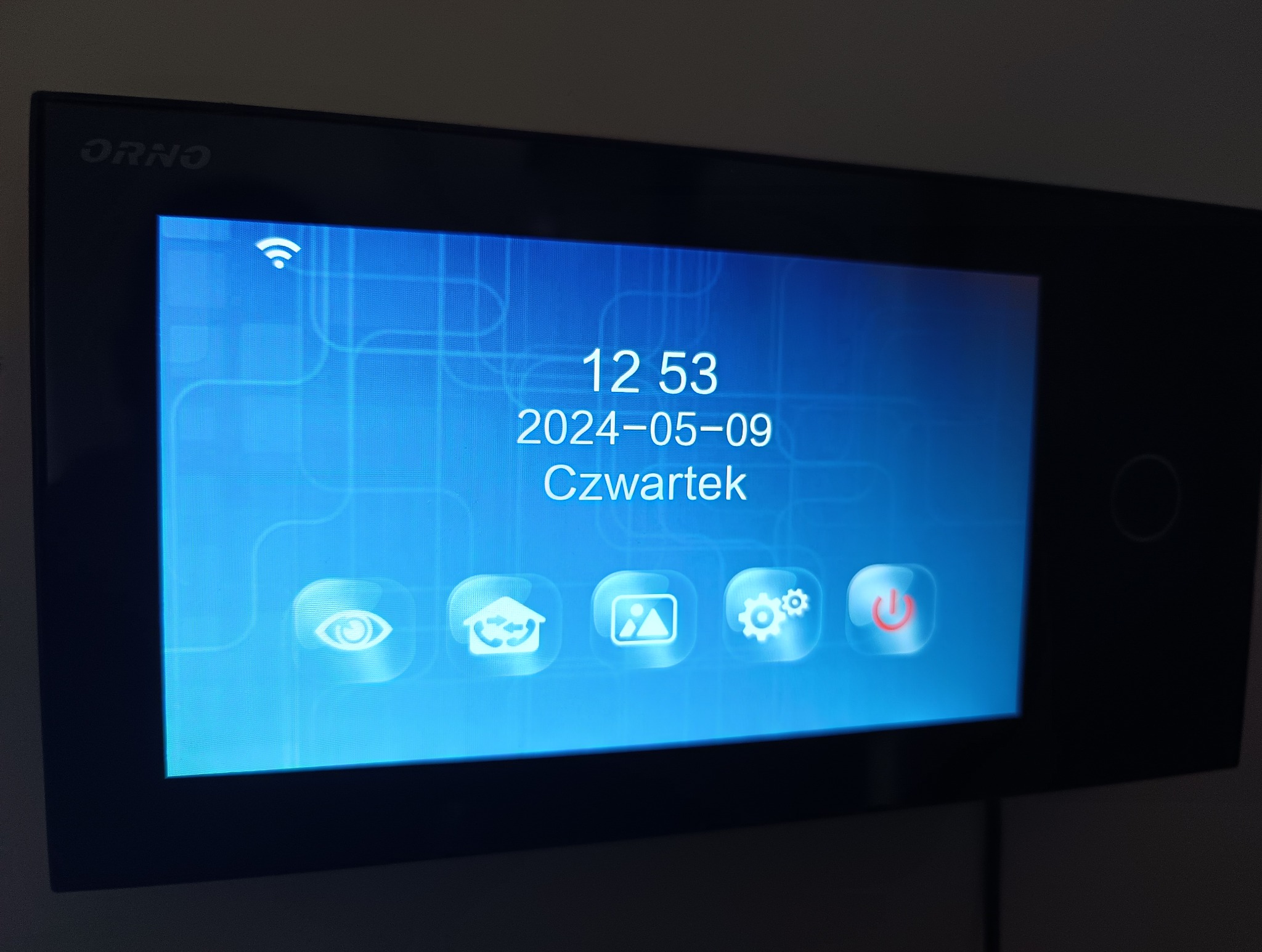 Ekran dotykowy wideodomofonu marki ORNO, wyświetlający datę 9 maja 2024, godzinę 12:53 oraz ikonę Wi-Fi i kilka ikon funkcyjnych.
