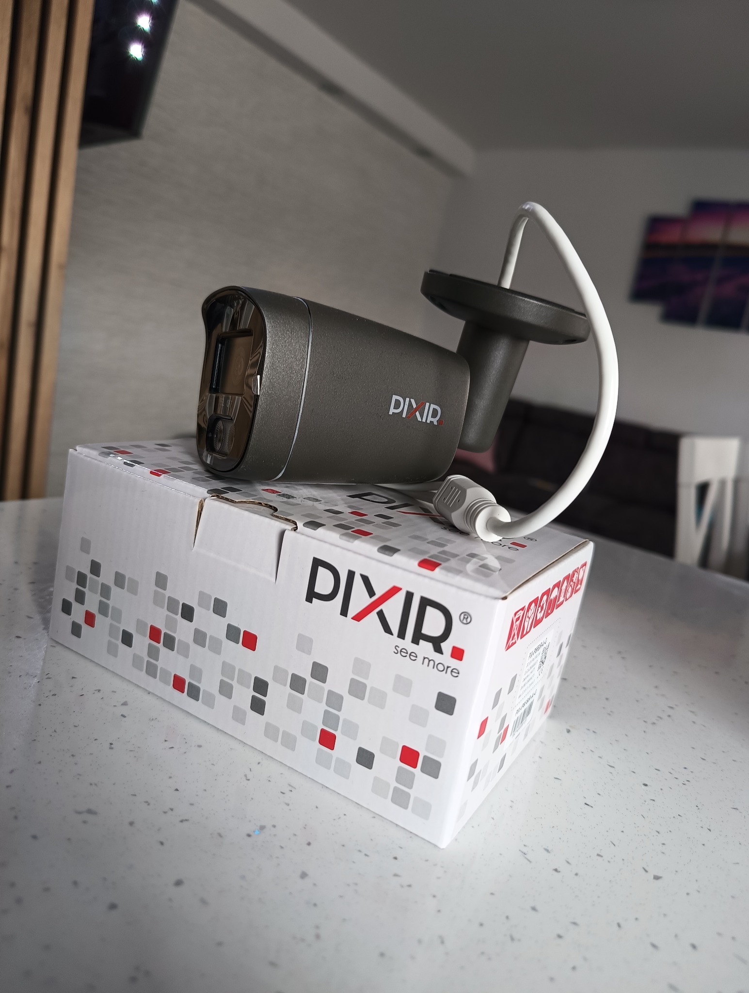 Kamera monitoringu Pixir na pudełku z logo firmy, widoczny kabel i uchwyt montażowy.