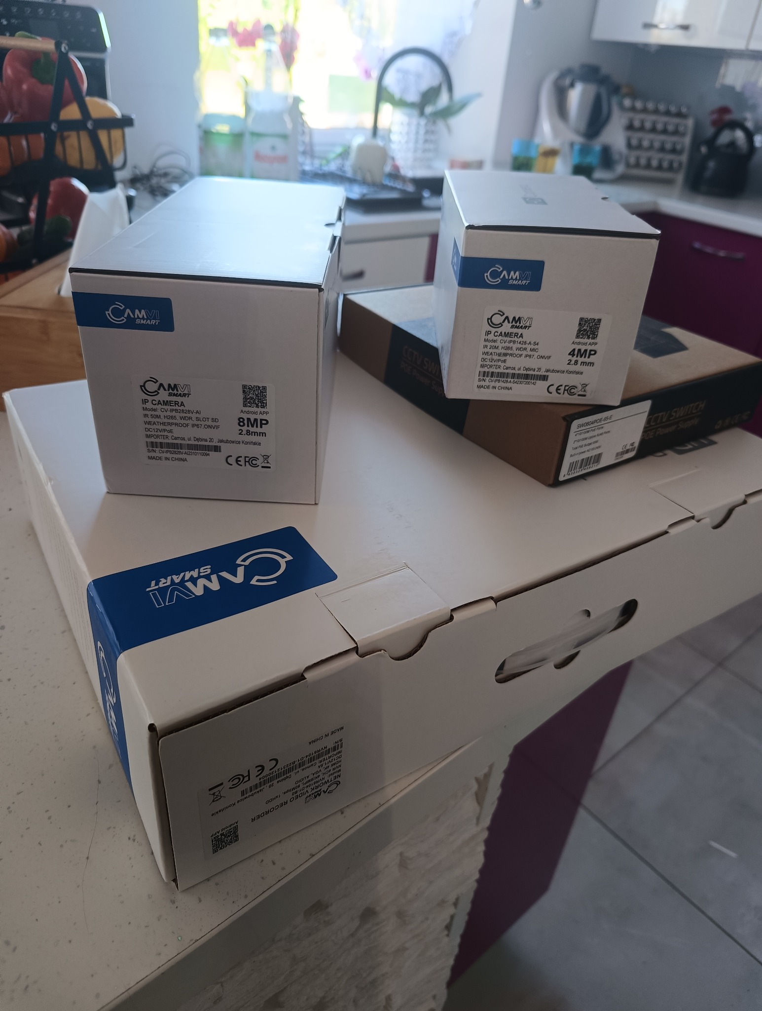 Pudełka z kamerami IP i rejestratorem wideo marki Camvi Smart na blacie kuchennym, widoczne specyfikacje techniczne i logo producenta.