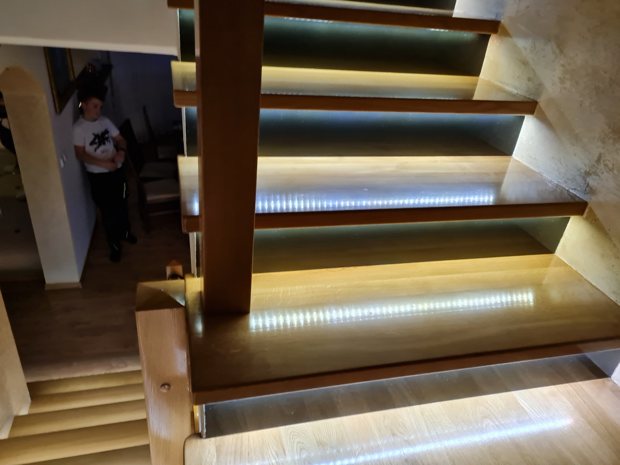 Nowoczesne schody z podświetlanymi stopniami, drewniane wykończenie, widok z góry na dół, osoba w tle.