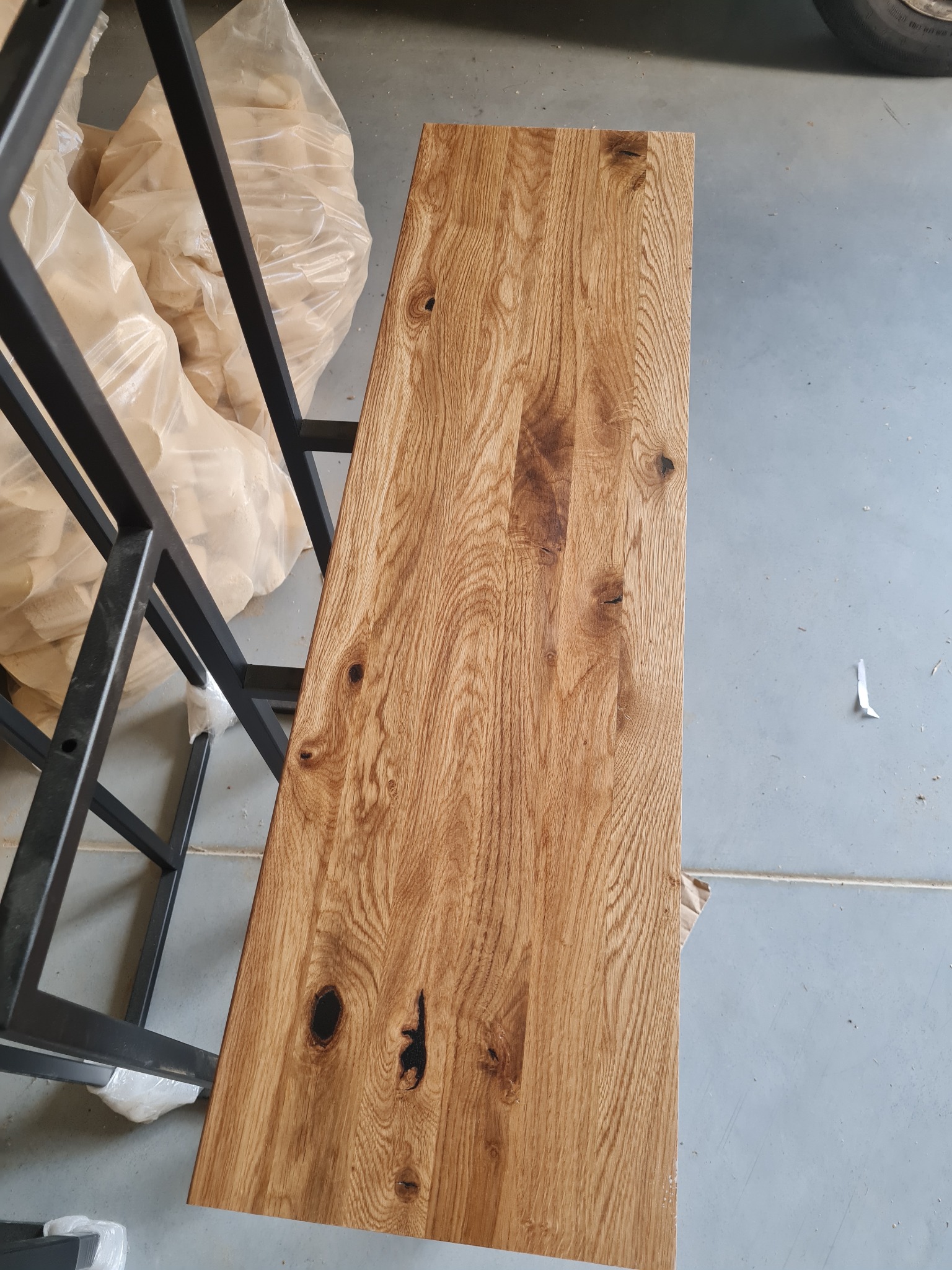 Surowy blat z litego drewna dębowego z wyraźnym usłojeniem i sękami, oparty na metalowej konstrukcji w warsztacie, widoczne zabezpieczone elementy pod blatem.