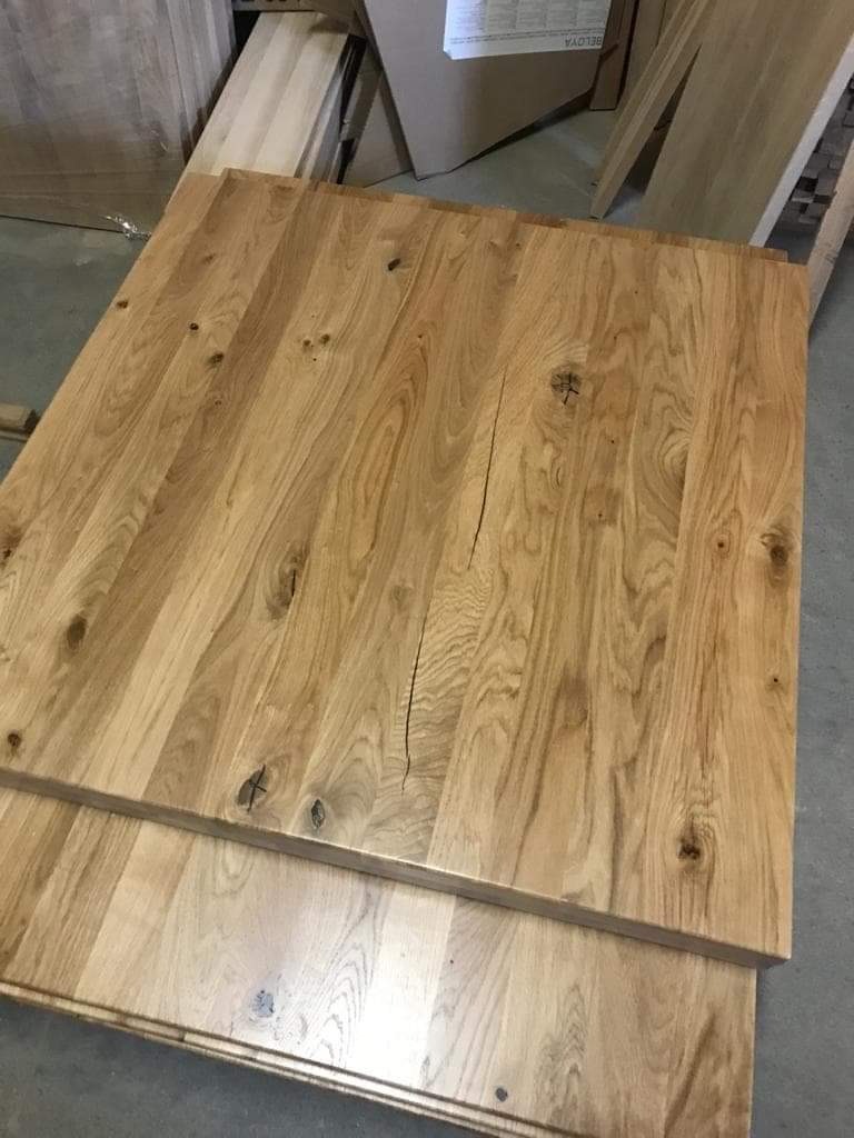Dwa blaty z jasnego drewna dębowego z widocznymi sękami i pęknięciami, ułożone jeden na drugim w warsztacie.