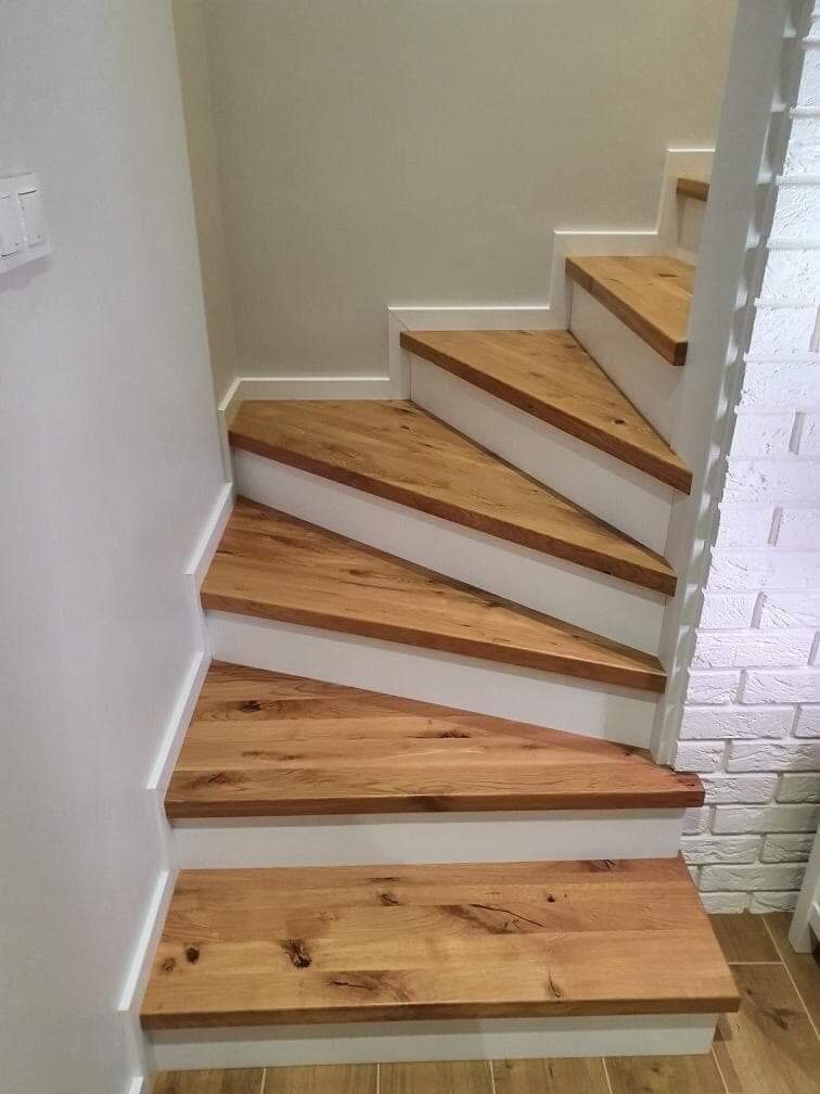 Stopnie z jasnego drewna dębowego z białymi podstopnicami, przy ścianie z białej cegły, widok z dołu na górę.