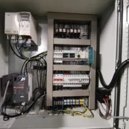 Otwarta szafa sterownicza z widocznymi elementami elektrycznymi: falownik ABB, bezpieczniki, przekaźniki, zasilacz impulsowy Mean Well EDR-150-24, oraz okablowanie.