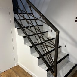 Weld Service - Nowoczesne schody z metalową balustradą o geometrycznym wzorze, wykończone białym marmurem z czarnymi akcentami, na tle drewnianej podłogi i białych ścian.