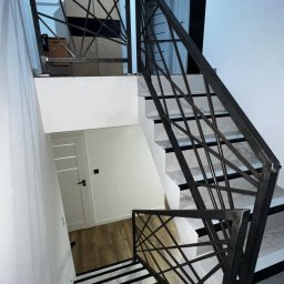 Weld Service - Nowoczesne schody z metalową balustradą o geometrycznym wzorze, białe ściany i marmurowe stopnie z czarnymi paskami, widok z góry.