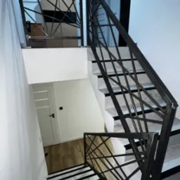 Nowoczesne schody z metalową balustradą o geometrycznym wzorze, białe ściany i marmurowe stopnie z czarnymi paskami, widok z góry.