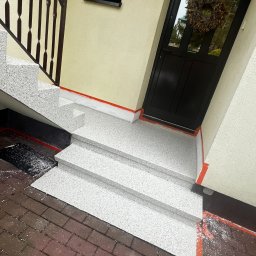 Dariusz Kulig usługi Remontowo-Budowlane - Wykończone schody zewnętrzne z żywicy Sika Floor. Widoczne trzy stopnie, balustrada, drzwi wejściowe z wieńcem i fragment chodnika z kostki. Detal wykończenia.