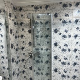 Dariusz Kulig usługi Remontowo-Budowlane - Kabina prysznicowa z wzorzystymi, kwiatowymi płytkami w odcieniach szarości i bieli. Widoczny fragment umywalki. Nowoczesny design łazienki po remoncie.