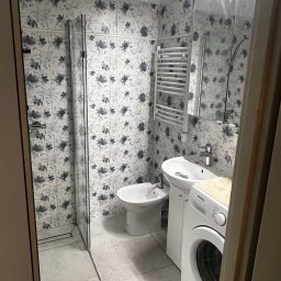 Dariusz Kulig usługi Remontowo-Budowlane - Ukończona łazienka z kabiną prysznicową, bidetem, umywalką i pralką. Ściany wyłożone płytkami w kwiatowy wzór. Minimalistyczny grzejnik drabinkowy.