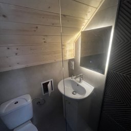 Dariusz Kulig usługi Remontowo-Budowlane - Nowoczesna łazienka na poddaszu z drewnianym sufitem, umywalką na postumencie, podświetlanym lustrem i toaletą. Ściana wykończona płytkami z geometrycznym wzorem.