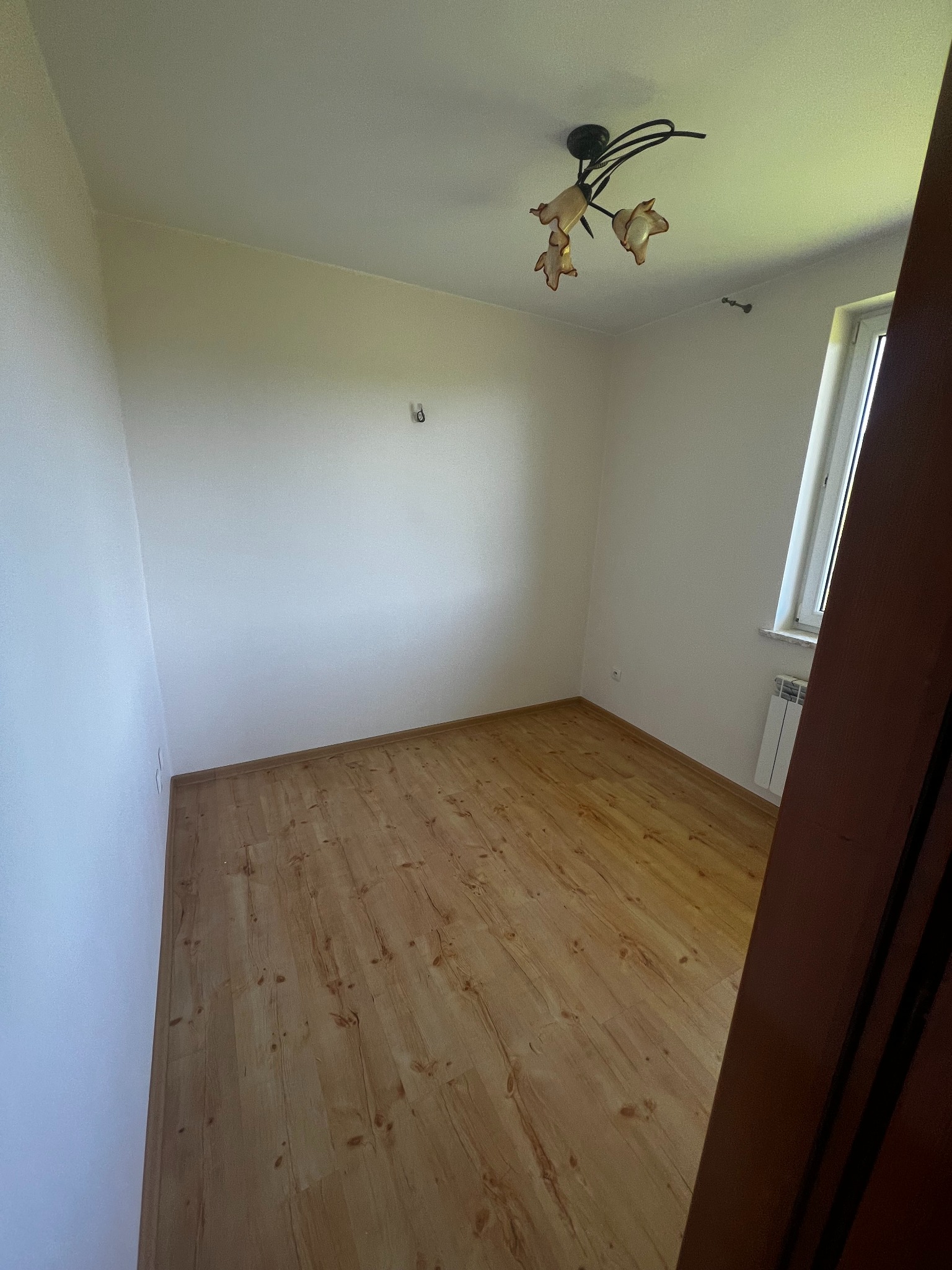 Jasne wnętrze pokoju po malowaniu ścian i położeniu paneli podłogowych. Widoczny grzejnik, okno i lampa sufitowa. Ukończone wykończenie.