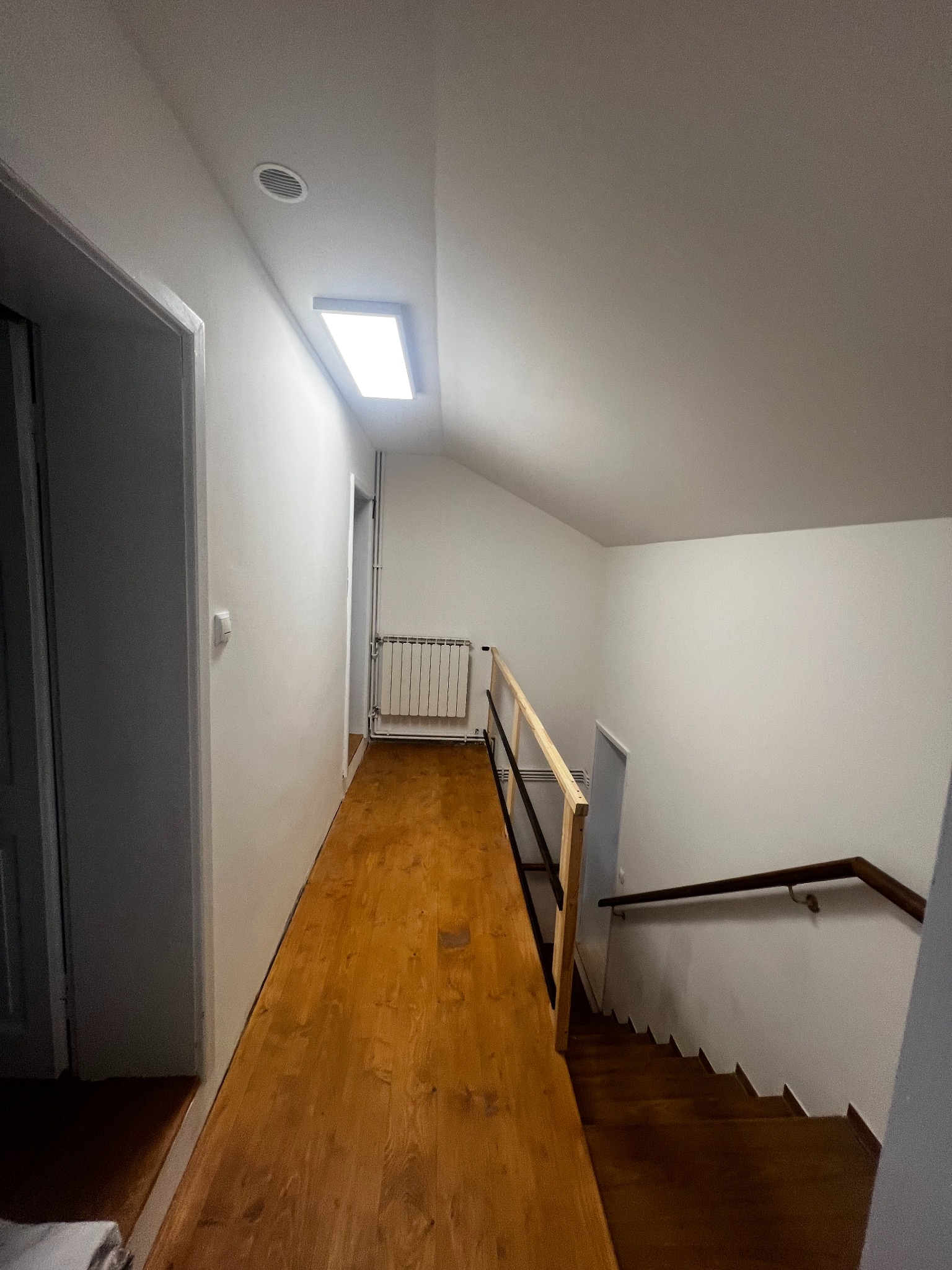 Wykończone poddasze w Sądku: drewniana podłoga, białe ściany, schody z balustradą. Widok z góry, oświetlenie sufitowe.