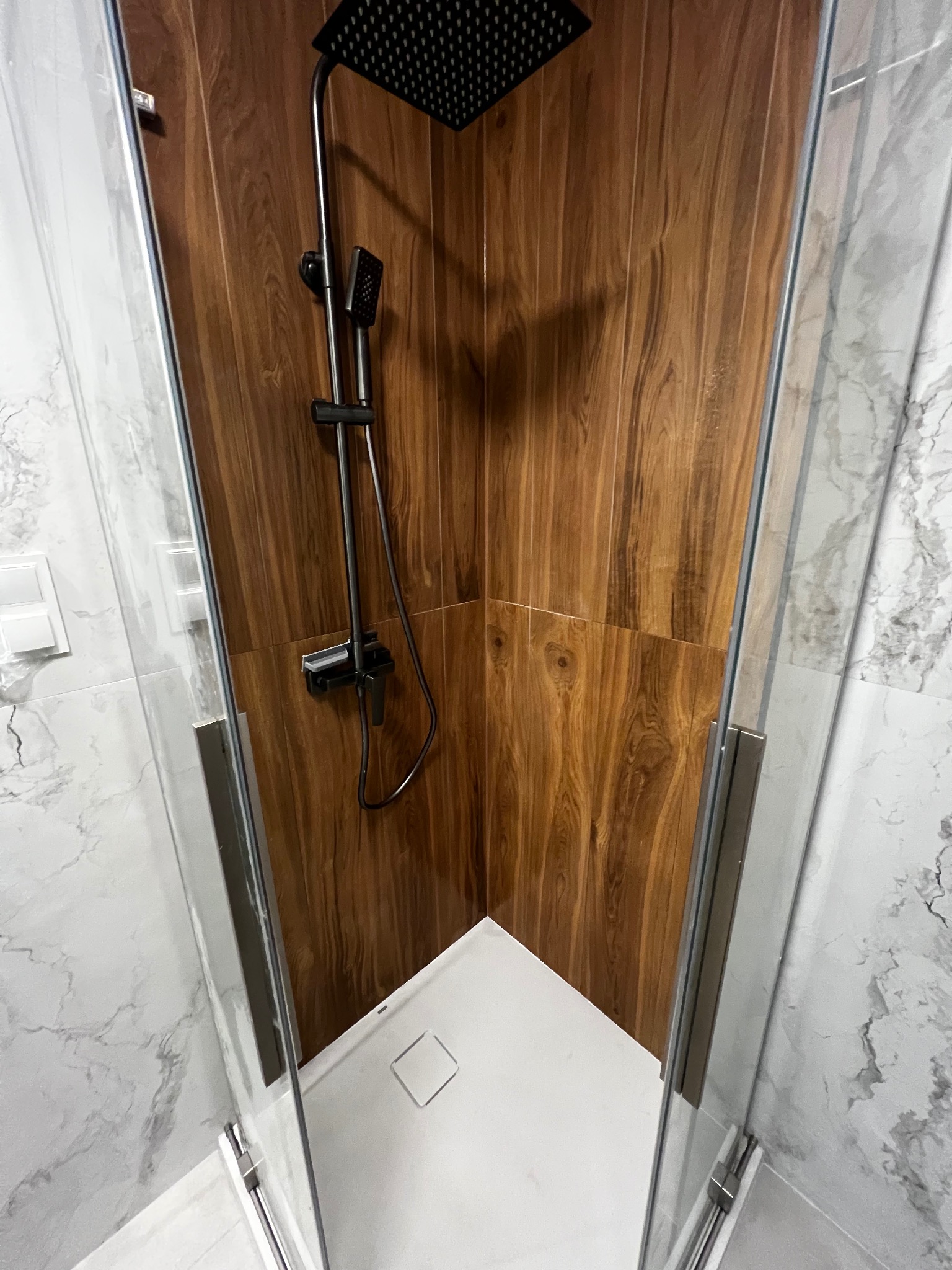 Kabina prysznicowa z deszczownicą i panelami imitującymi drewno, wykończona marmurowymi płytkami. Nowoczesny design z minimalistycznym odpływem liniowym.