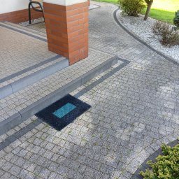 KJB cleaning - Szara kostka brukowa przed domem z zielonym dywanikiem i elementami architektury ogrodowej. Widoczne zabrudzenia i mech w spoinach kostki.