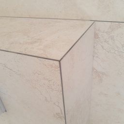 Robert Śniadach - Detal wykończenia narożnika z płytek ceramicznych w beżowym odcieniu, z widocznymi fugami i delikatnym wzorem imitującym kamień.