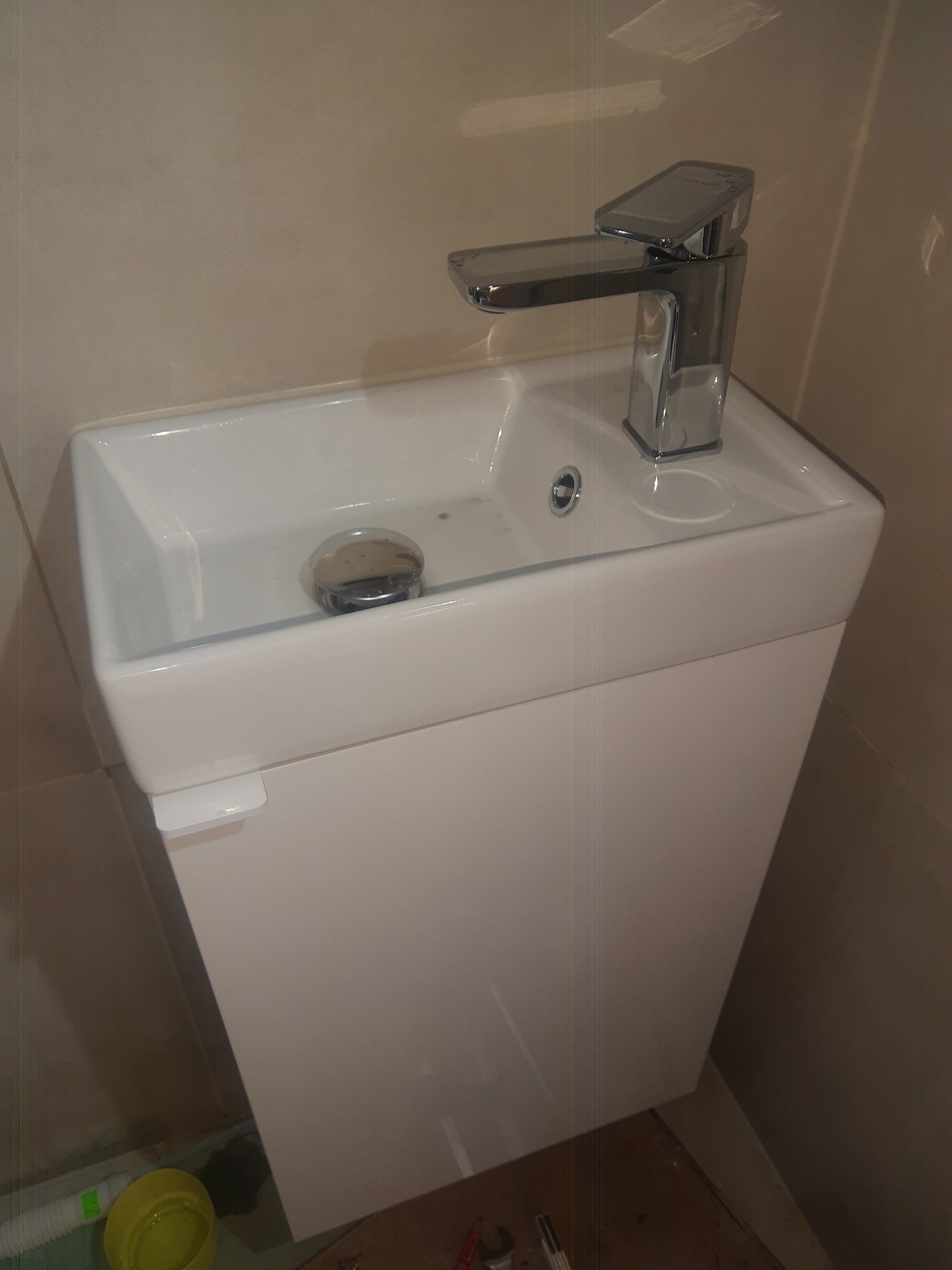 Wąska, biała umywalka z szafką i nowoczesną, chromowaną baterią zamontowana w łazience z beżowymi płytkami.