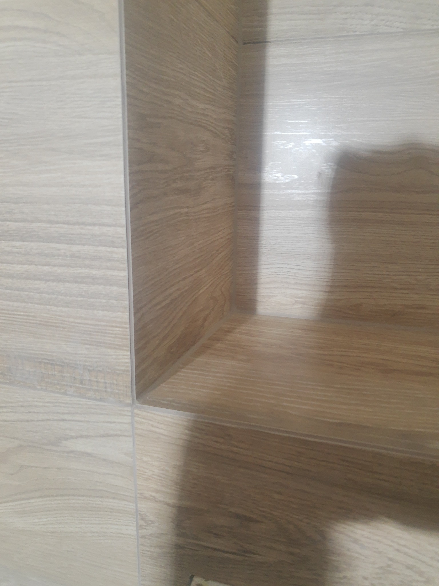 Półka wnękowa w łazience wyłożona płytkami imitującymi drewno, jasne i ciemne odcienie, widoczne fugi.