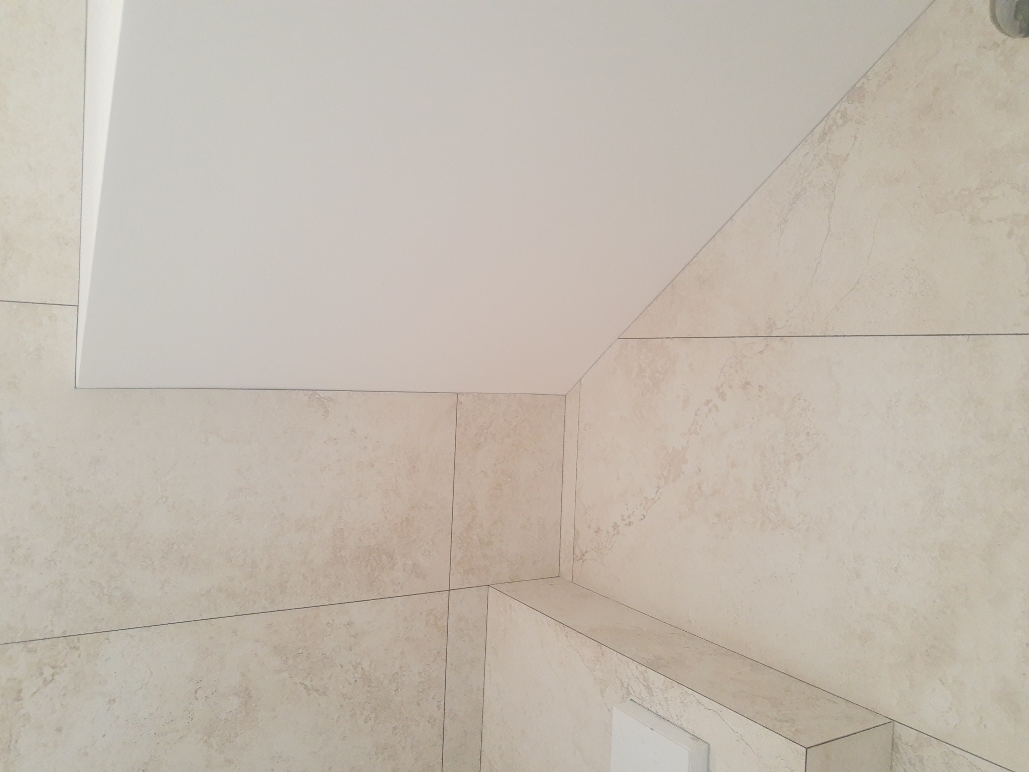 Wykończona łazienka z beżowymi płytkami imitującymi kamień, z widocznym narożnikiem i podwieszanym sufitem