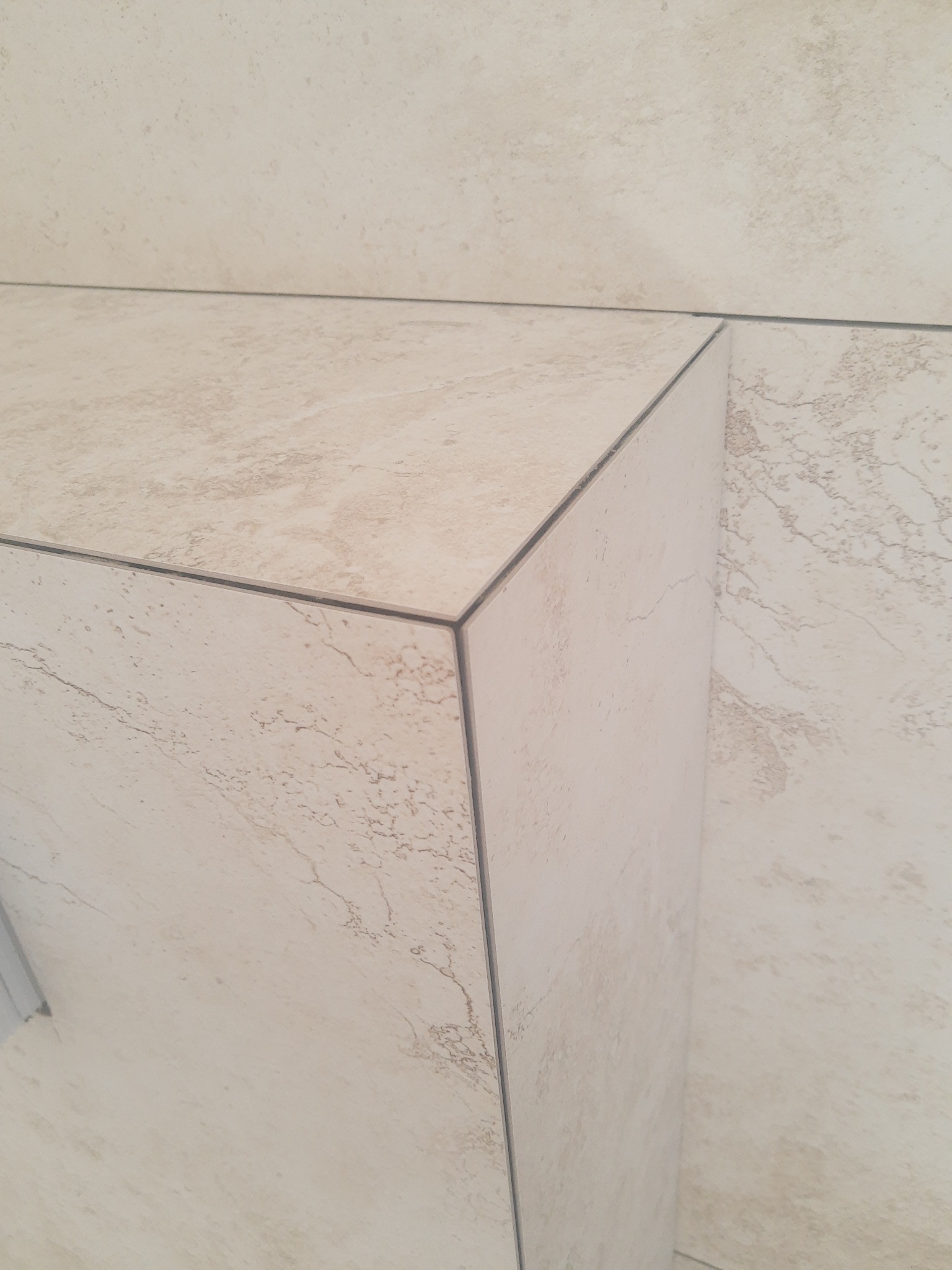 Detal wykończenia narożnika z płytek ceramicznych w beżowym odcieniu, z widocznymi fugami i delikatnym wzorem imitującym kamień.