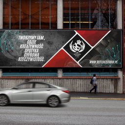 Reflekz Studio - Billboard reklamowy z hasłem 'Tworzymy tam, gdzie kreatywność spotyka cyfrowa rzeczywistość' i logo Reflekz Studio, umieszczony na budynku w miejskiej scenerii. Rozmyty samochód i przechodzień...