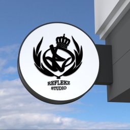 Reflekz Studio - Okrągły szyld reklamowy z czarnym logo firmy 'Reflekz Studio' przedstawiającym stylizowaną literę R z koroną, zamontowany na elewacji budynku na tle błękitnego nieba z chmurami.