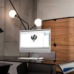 Reflekz Studio - Monitor wyświetla projekt logo z koroną i stylizowaną sylwetką sportowca, widoczny na nowoczesnym biurku z czarnym blatem i designerską lampą, na tle betonowej ściany i drewnianej komody.