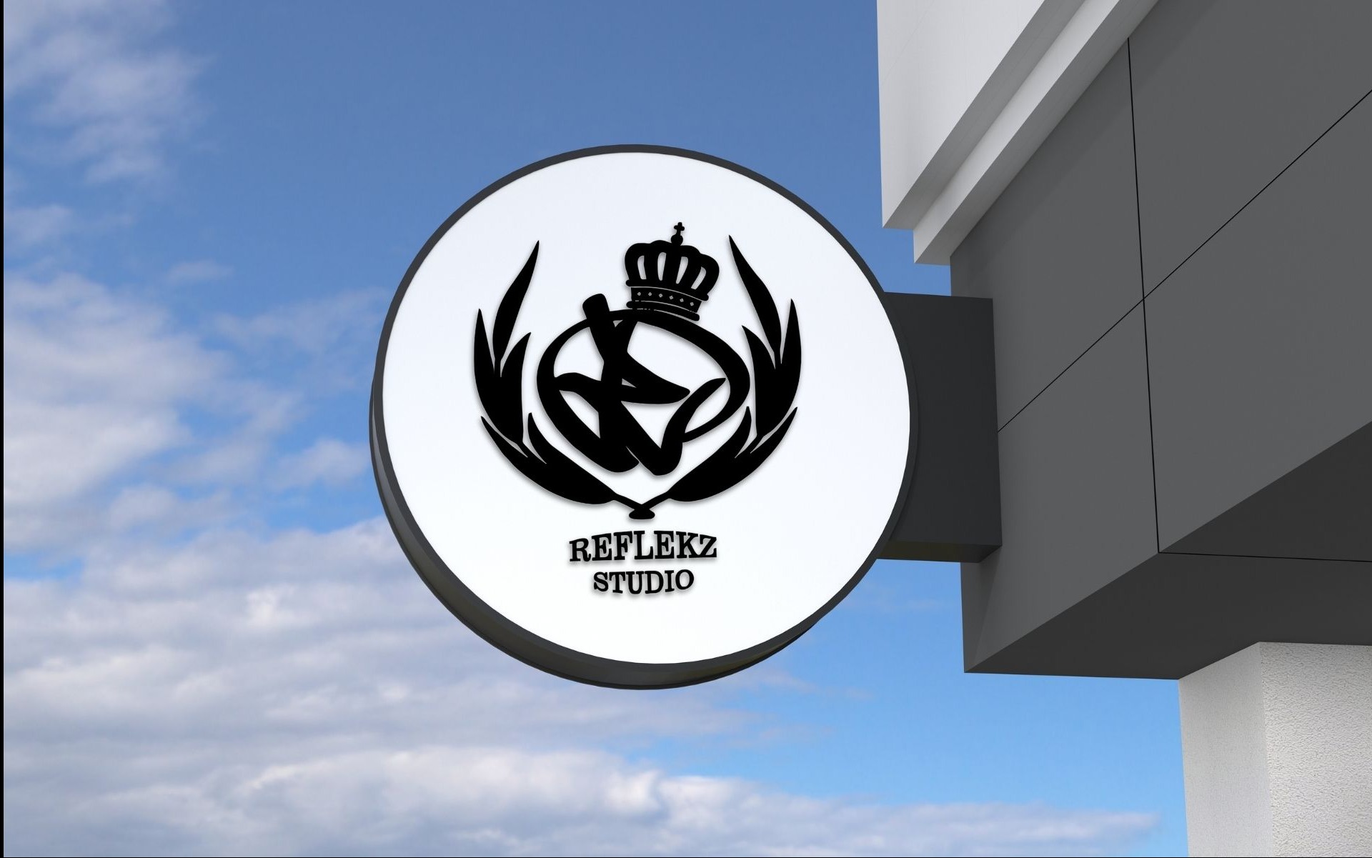 Okrągły szyld reklamowy z czarnym logo firmy 'Reflekz Studio' przedstawiającym stylizowaną literę R z koroną, zamontowany na elewacji budynku na tle błękitnego nieba z chmurami.