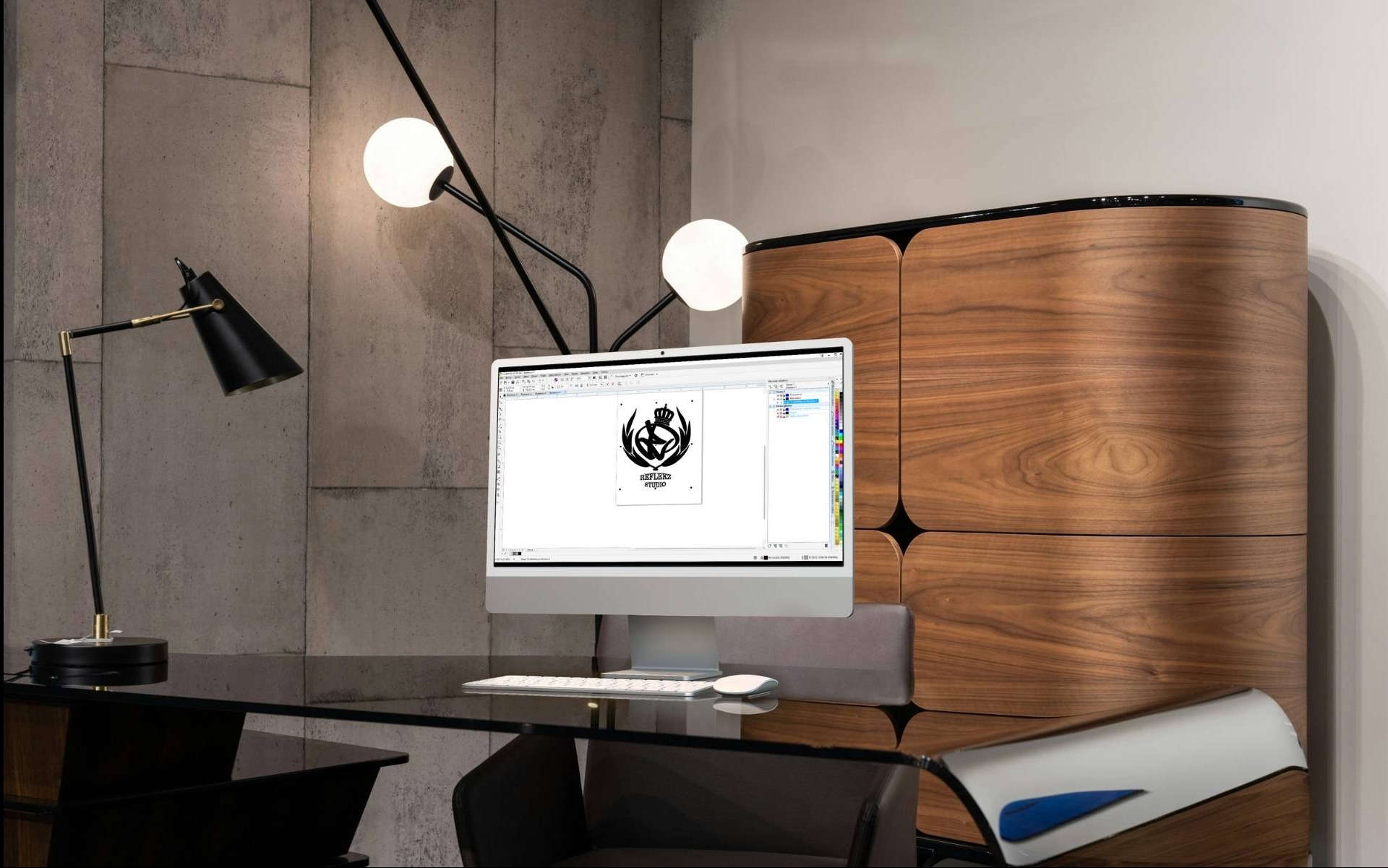 Monitor wyświetla projekt logo z koroną i stylizowaną sylwetką sportowca, widoczny na nowoczesnym biurku z czarnym blatem i designerską lampą, na tle betonowej ściany i drewnianej komody.