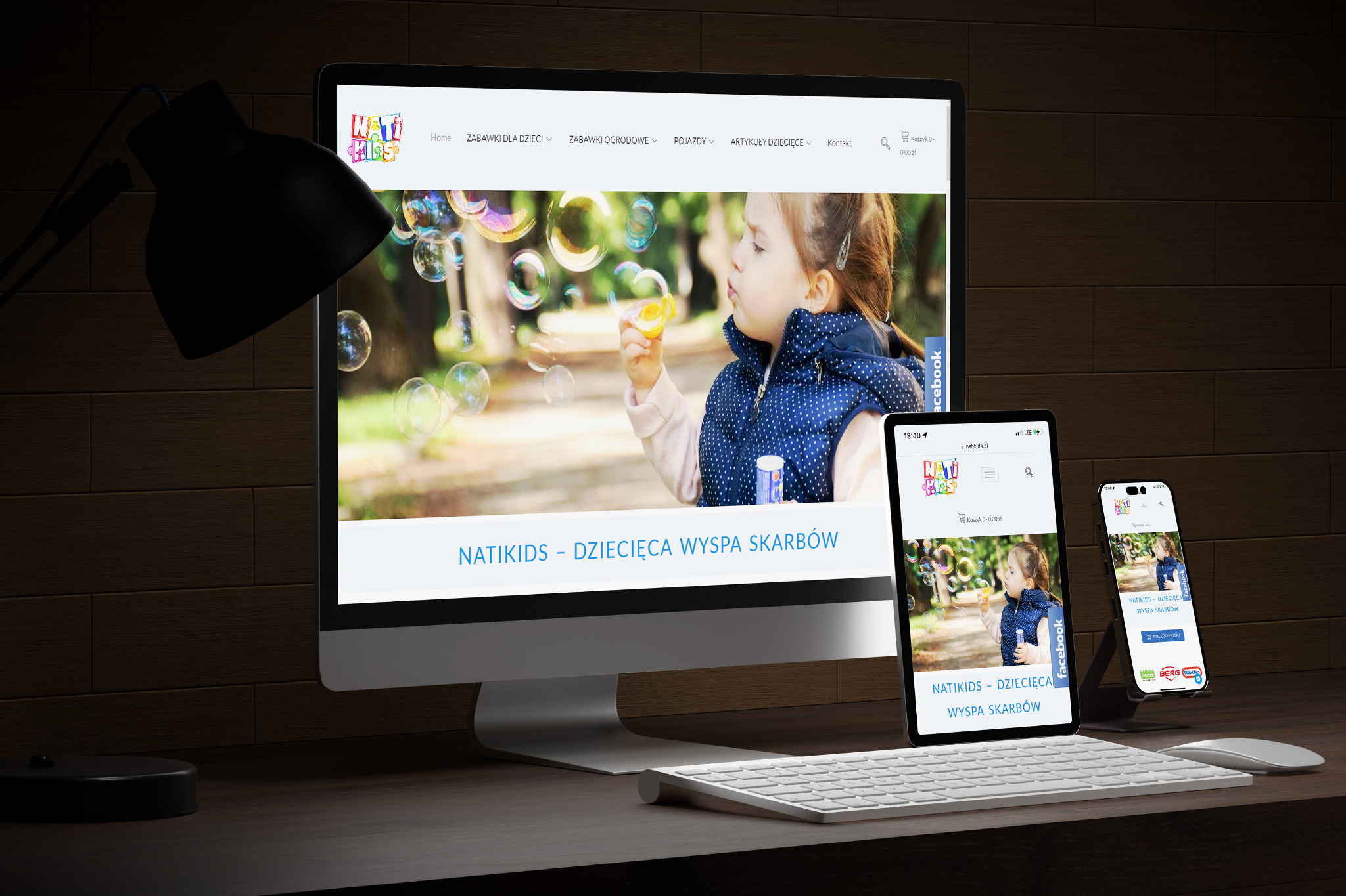 Responsywna strona internetowa sklepu z zabawkami NatiKids wyświetlana na monitorze, tablecie i telefonie, na tle biurka z lampką.