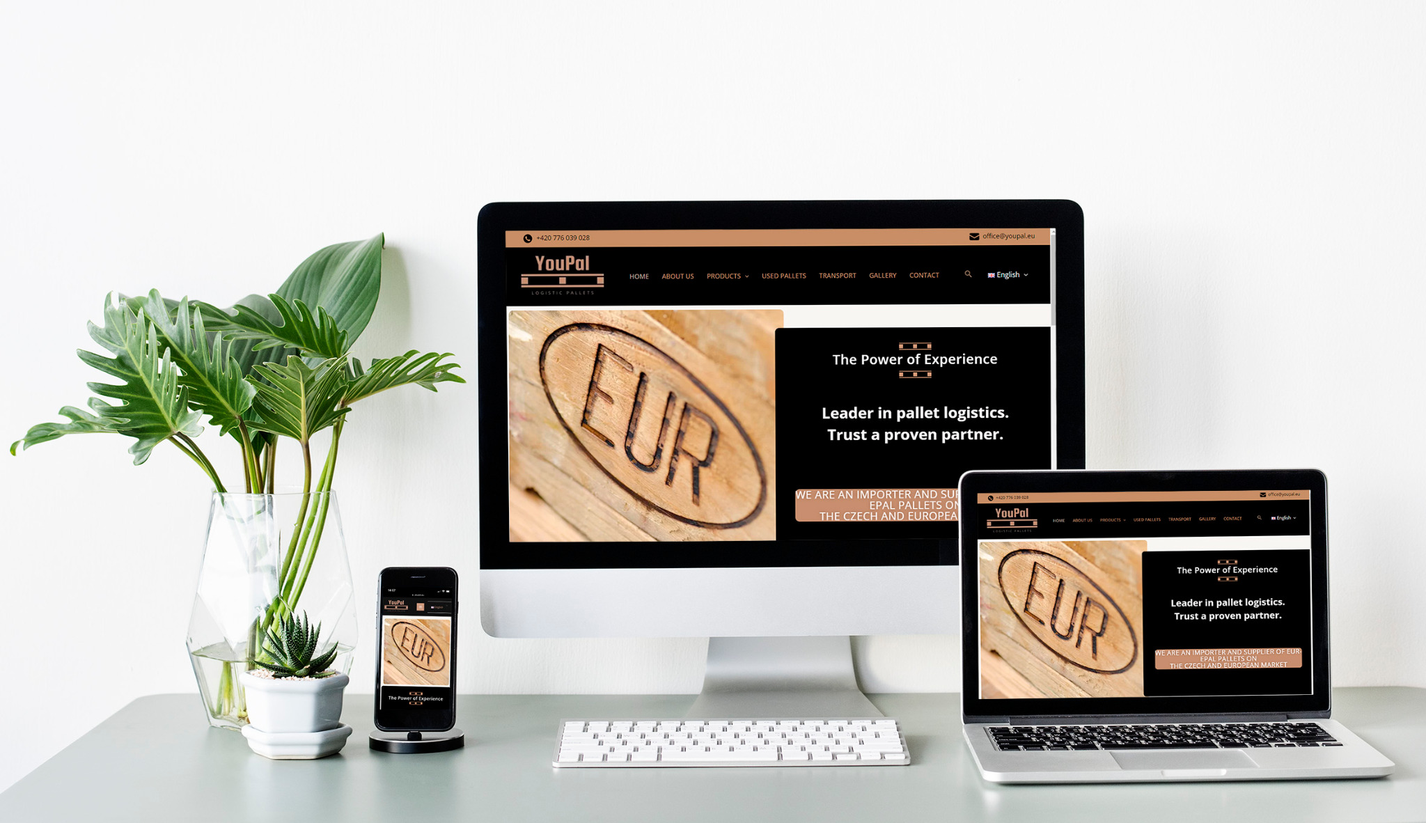 Responsywna strona internetowa firmy logistycznej YouPal wyświetlana na monitorze, laptopie i smartfonie, obok roślin doniczkowych na biurku.