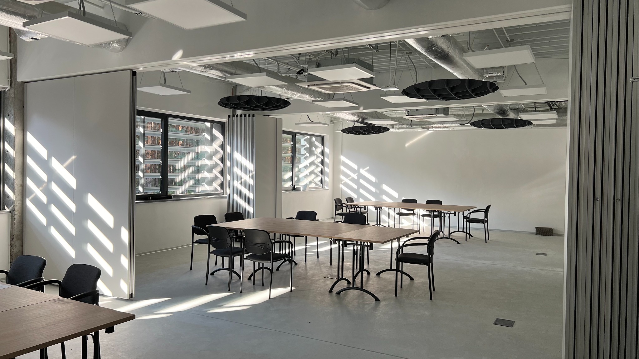 Jasne biuro we Wrocławiu po remoncie, widoczne stoły konferencyjne z krzesłami, nowoczesne oświetlenie sufitowe i wpadające promienie słoneczne przez okna.