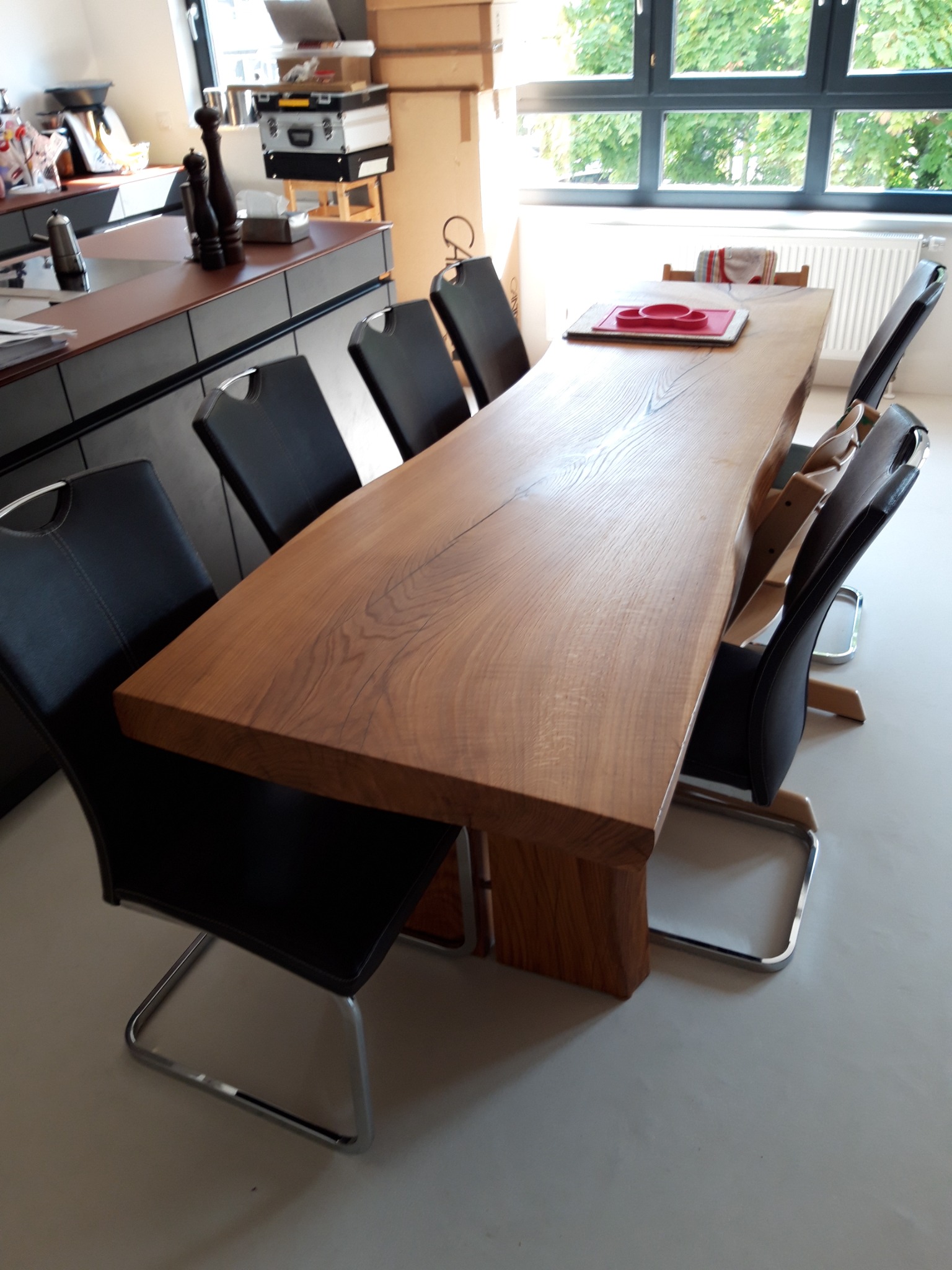 Stół z litego drewna o nieregularnych krawędziach, otoczony czarnymi krzesłami z metalowymi nogami w nowoczesnej jadalni z dużym oknem.