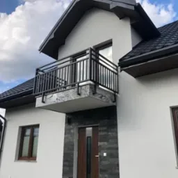 Nowoczesna, czarna balustrada balkonowa z prostych profili, zamontowana w domu we Włoszczowie, z elewacją wykończoną szarym kamieniem dekoracyjnym.