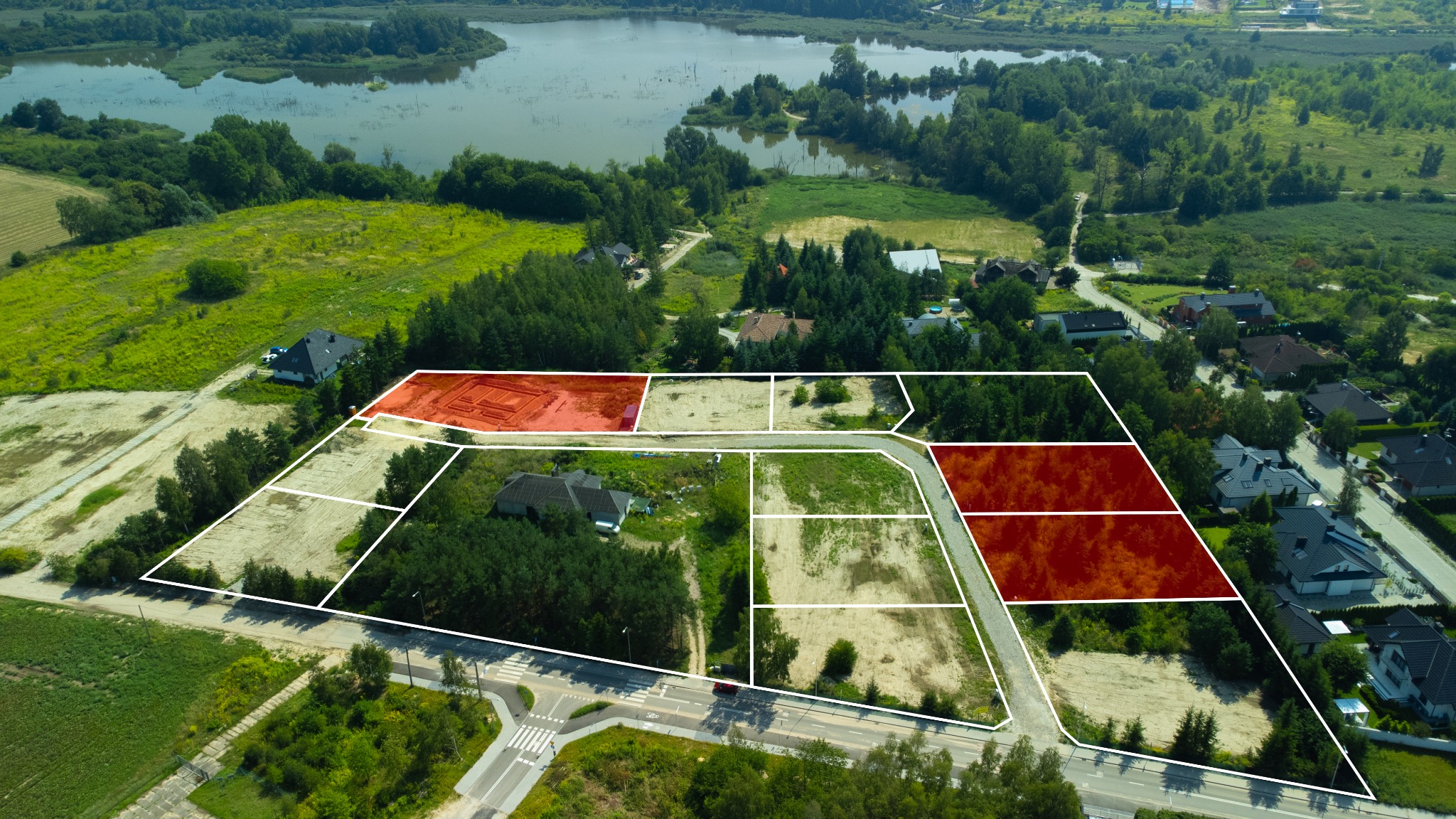 Widok z lotu ptaka na działki budowlane z zaznaczonymi granicami, w tle jezioro i tereny zielone.